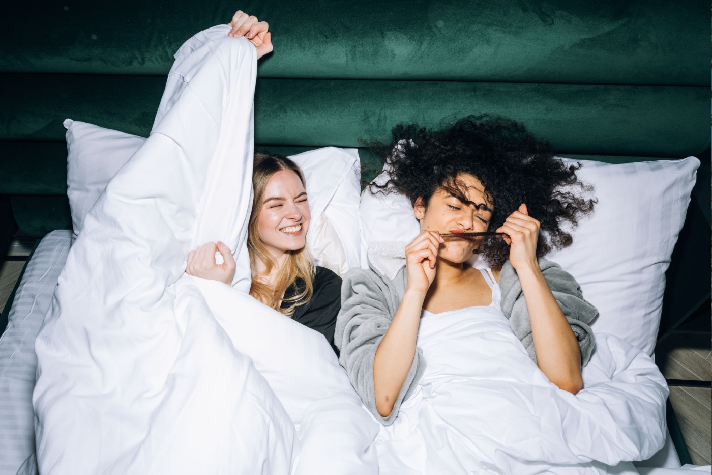 Zwei Freundinnen lachen in einem Hotelbett